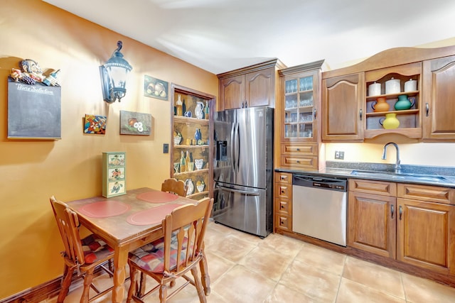 kitchen featuring dark countertops, light tile patterned floors, appliances with stainless steel finishes, brown cabinetry, and a sink