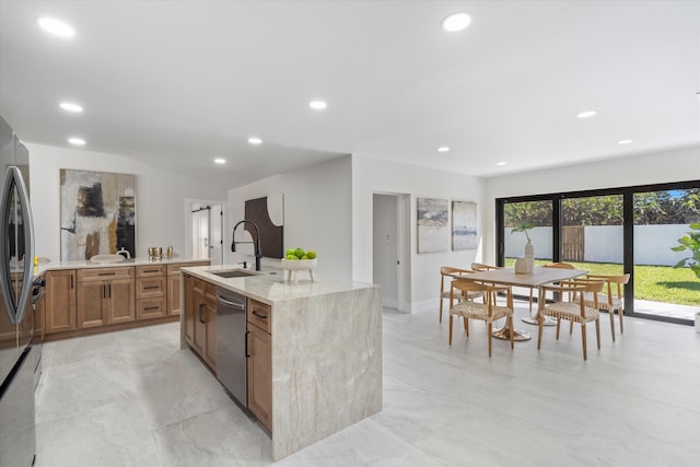 kitchen with a center island with sink, recessed lighting, a sink, appliances with stainless steel finishes, and brown cabinets