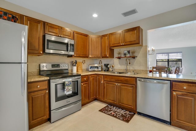 kitchen featuring brown cabinetry, visible vents, stainless steel appliances, and a sink