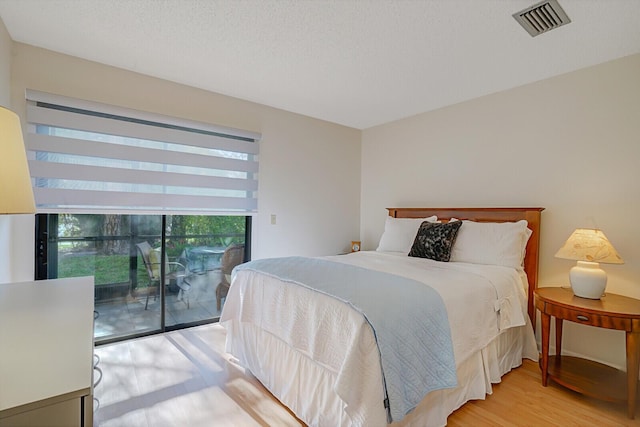 bedroom with access to exterior, light wood-style floors, visible vents, and a textured ceiling