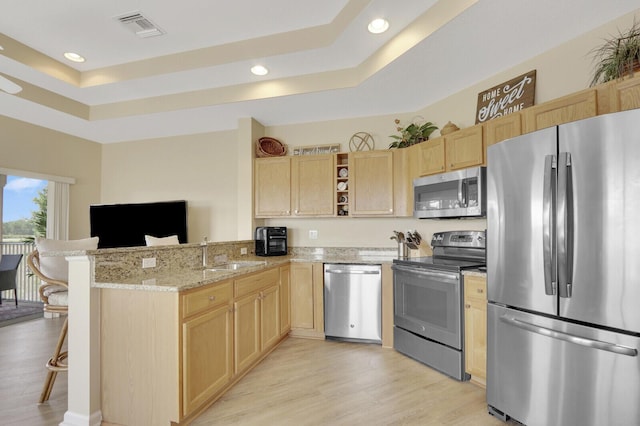 8290 Mulligan Cir Unit 2421, Port Saint Lucie, FL 34986 - kitchen with stainless steel appliances, light brown cabinetry, a sink, a raised ceiling, and a peninsula