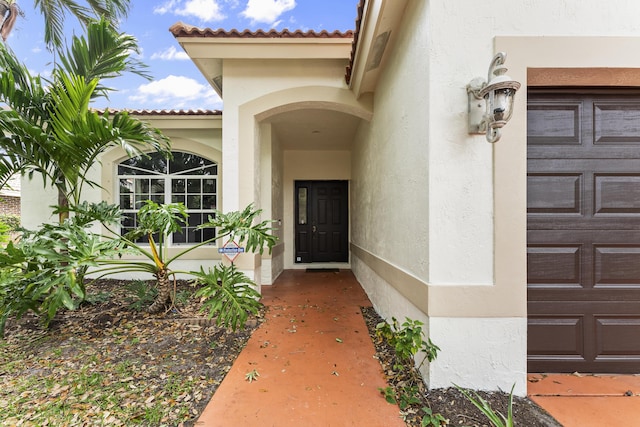 entrance to property featuring stucco siding, an attached garage, and a tile roof