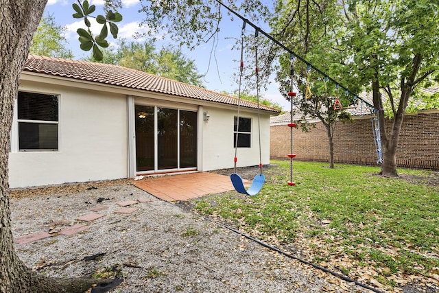 back of property featuring stucco siding, a tile roof, a lawn, and fence