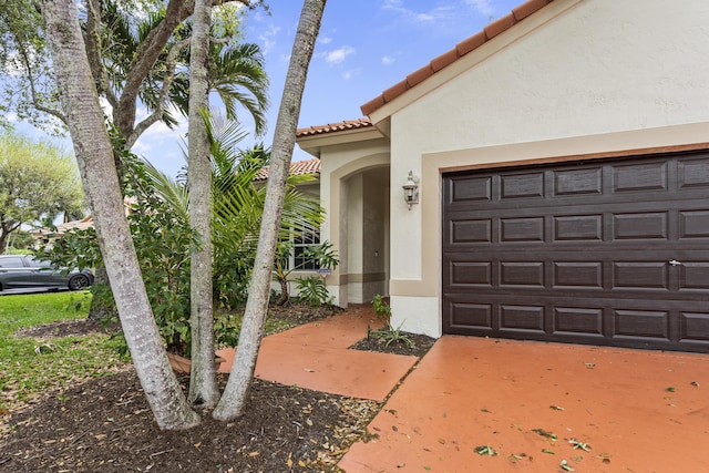 view of exterior entry featuring a tiled roof, an attached garage, and stucco siding