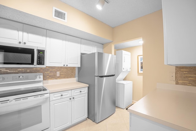 kitchen featuring visible vents, light tile patterned flooring, decorative backsplash, stacked washer and clothes dryer, and appliances with stainless steel finishes