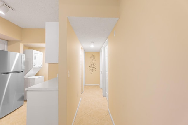 corridor featuring light tile patterned floors, a textured ceiling, and stacked washer and dryer