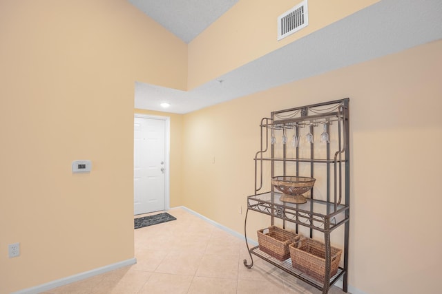 hallway with visible vents, baseboards, a textured ceiling, and light tile patterned flooring