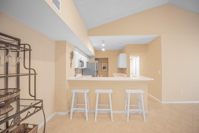 kitchen featuring visible vents, white cabinets, freestanding refrigerator, and lofted ceiling