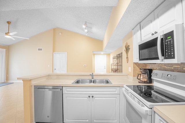 kitchen with a sink, white appliances, a peninsula, light countertops, and vaulted ceiling