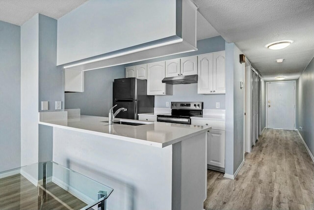 kitchen with under cabinet range hood, a sink, stainless steel electric stove, white cabinetry, and freestanding refrigerator