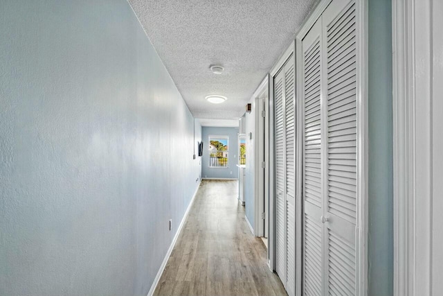 hall featuring baseboards, a textured ceiling, and light wood-style flooring