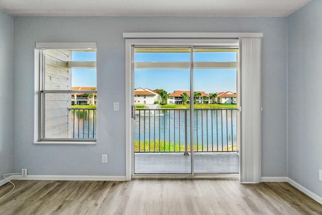 empty room featuring plenty of natural light, a water view, baseboards, and wood finished floors