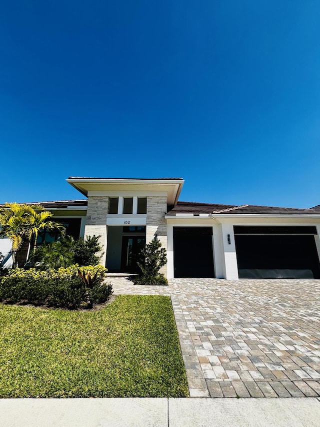 prairie-style home featuring a front yard, stucco siding, a garage, stone siding, and decorative driveway