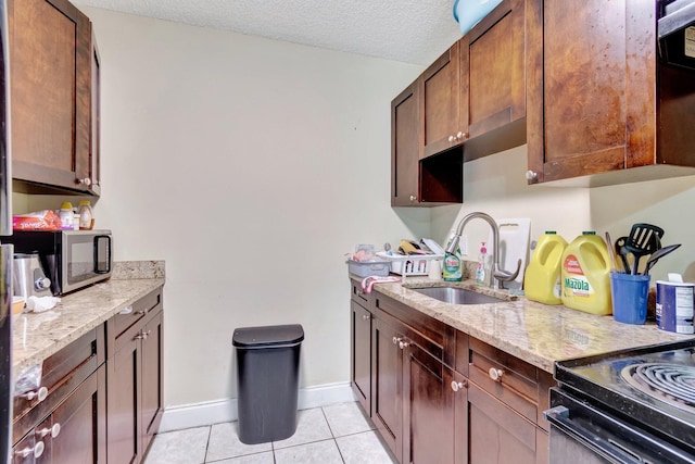 kitchen with light stone countertops, light tile patterned flooring, a sink, a textured ceiling, and stainless steel microwave