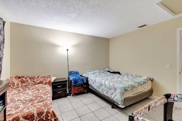 bedroom featuring visible vents, a textured ceiling, attic access, and light tile patterned flooring