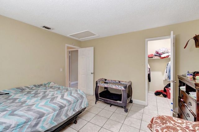 bedroom with a walk in closet, attic access, a closet, light tile patterned flooring, and a textured ceiling