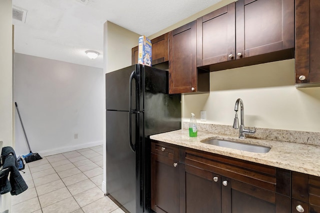 kitchen featuring visible vents, dark brown cabinets, light tile patterned floors, freestanding refrigerator, and a sink