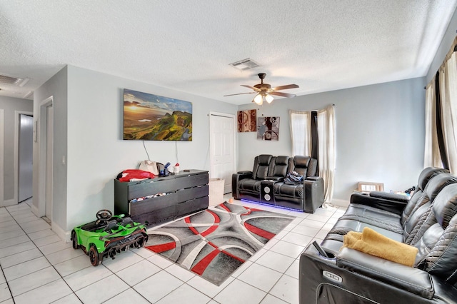 living area with tile patterned flooring, a ceiling fan, visible vents, and a textured ceiling