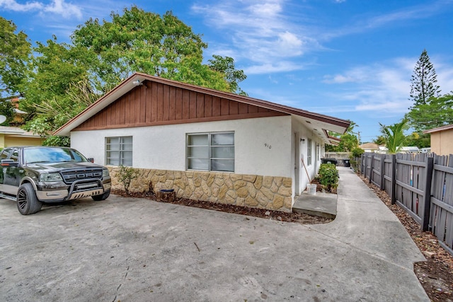 view of front facade featuring stone siding, stucco siding, and fence