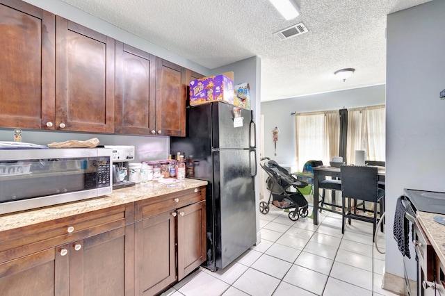 kitchen with visible vents, light stone counters, a textured ceiling, stainless steel appliances, and light tile patterned floors