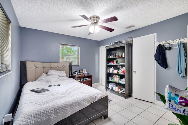 bedroom featuring visible vents, a textured ceiling, light tile patterned flooring, baseboards, and ceiling fan