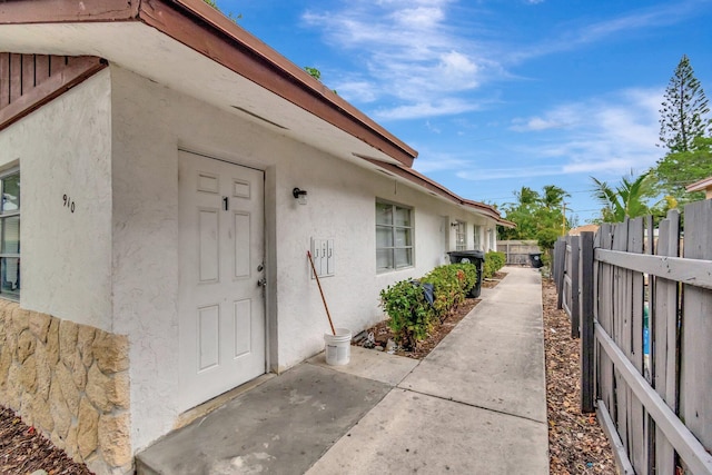 view of exterior entry featuring stucco siding, a patio, and fence