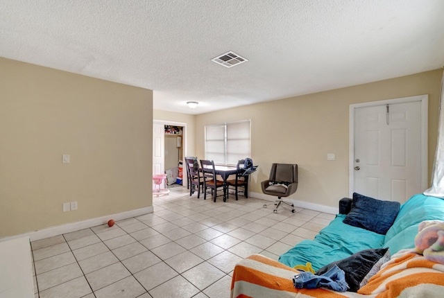 living room featuring light tile patterned flooring, visible vents, a textured ceiling, and baseboards