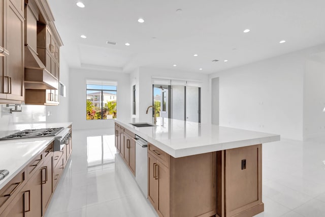 kitchen with recessed lighting, a large island with sink, stainless steel appliances, a sink, and wall chimney exhaust hood