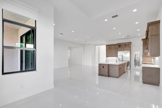 kitchen with a center island with sink, baseboards, recessed lighting, light countertops, and built in refrigerator