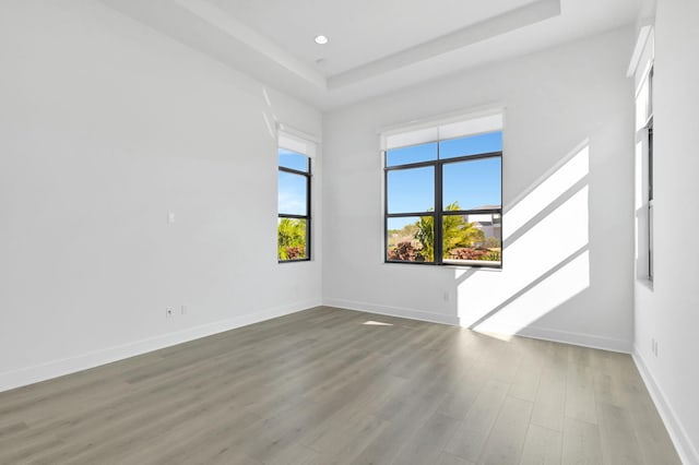 empty room with a raised ceiling, recessed lighting, wood finished floors, and baseboards