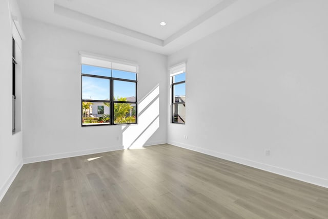 empty room featuring a raised ceiling, recessed lighting, wood finished floors, and baseboards