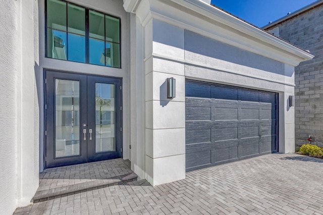 entrance to property featuring french doors, decorative driveway, an attached garage, and stucco siding