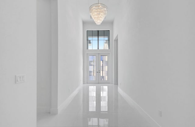 interior space with baseboards, tile patterned flooring, french doors, a towering ceiling, and a notable chandelier