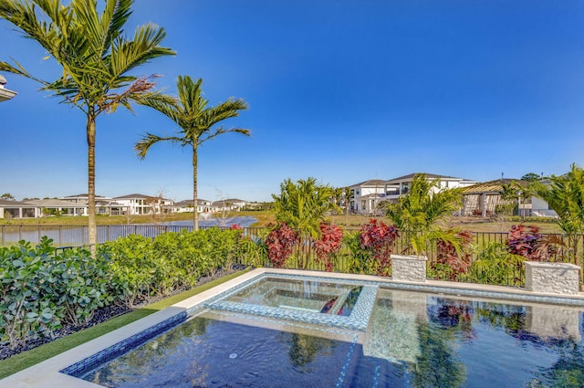 view of swimming pool with an in ground hot tub, a fenced backyard, and a water view