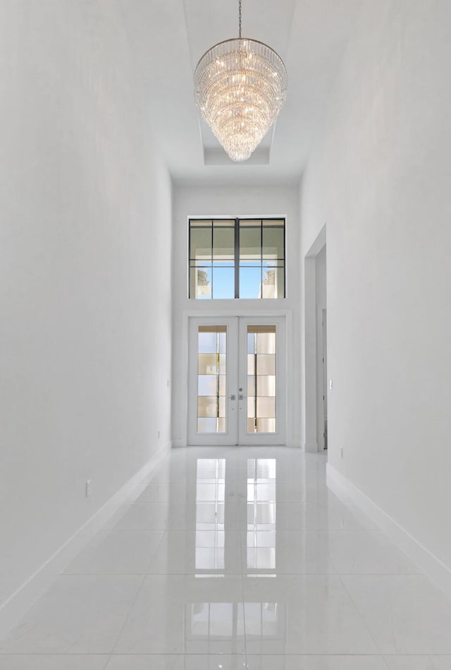 interior space with a notable chandelier, french doors, a high ceiling, and baseboards