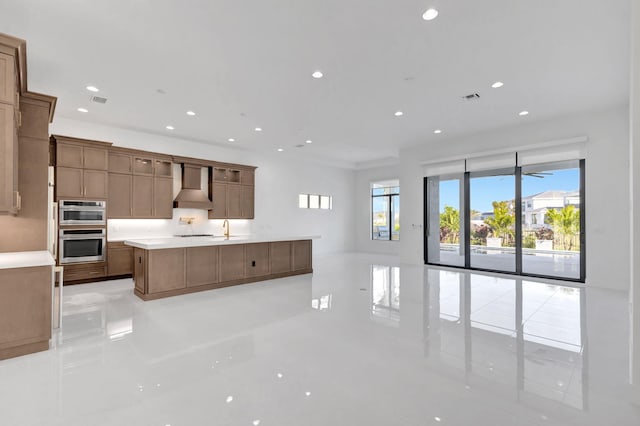 kitchen featuring stainless steel double oven, recessed lighting, light countertops, a large island, and wall chimney range hood