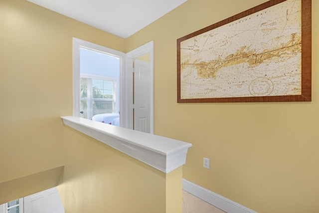 hallway featuring light tile patterned floors, an upstairs landing, and baseboards