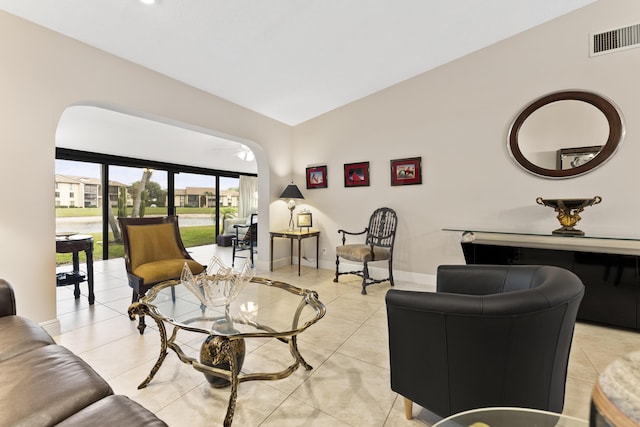 living room featuring visible vents, baseboards, lofted ceiling, light tile patterned floors, and arched walkways