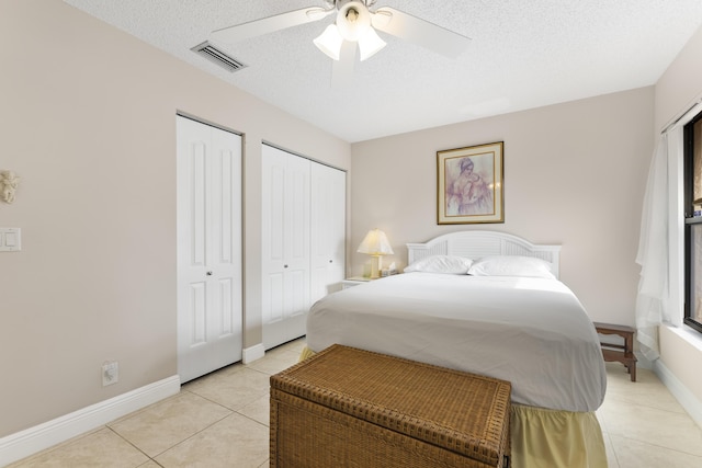 bedroom featuring visible vents, two closets, baseboards, light tile patterned flooring, and a textured ceiling