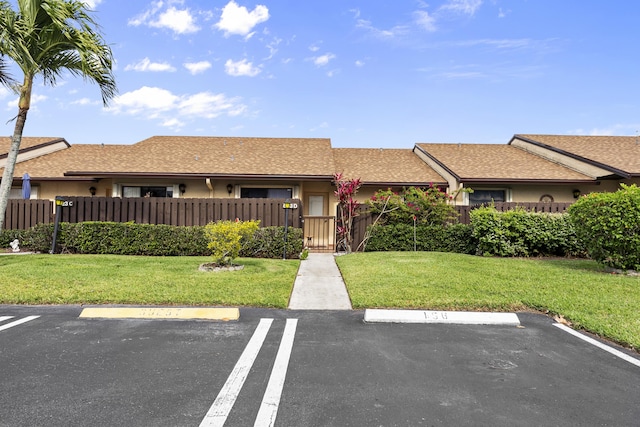 ranch-style home with a shingled roof, a front lawn, a fenced front yard, stucco siding, and uncovered parking