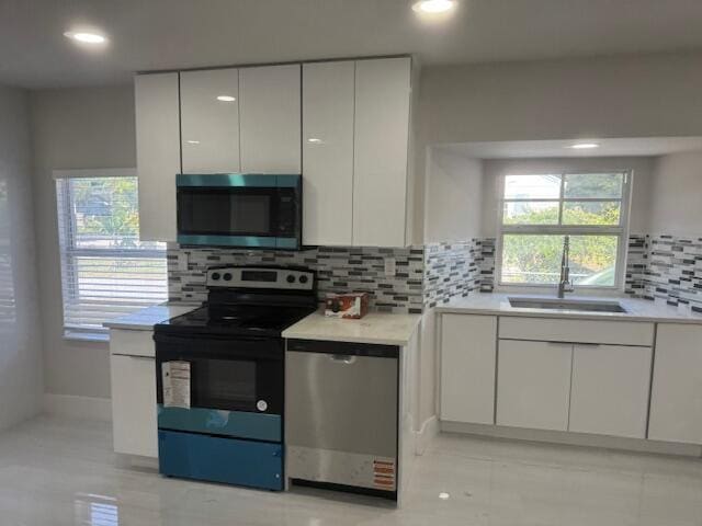 kitchen with a sink, backsplash, white cabinetry, stainless steel appliances, and light countertops