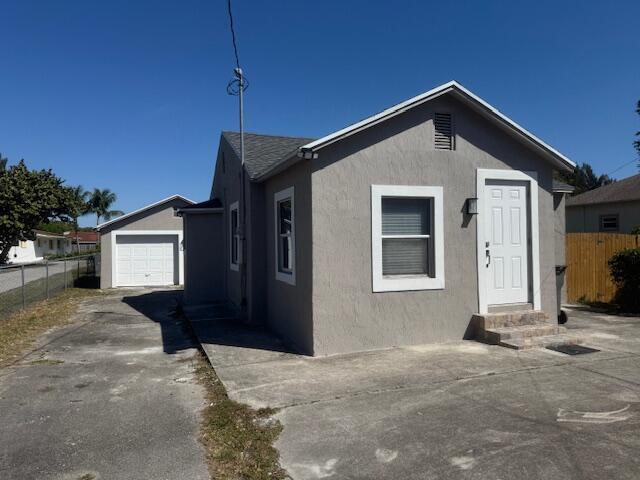 view of front facade with stucco siding, entry steps, driveway, and fence