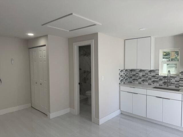 kitchen with baseboards, a sink, light countertops, white cabinetry, and backsplash