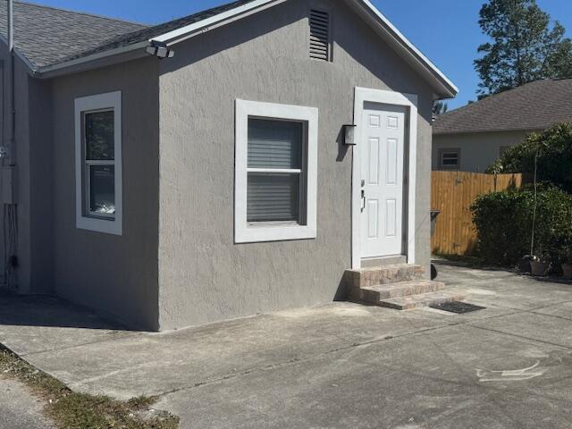 doorway to property featuring fence, roof with shingles, and stucco siding