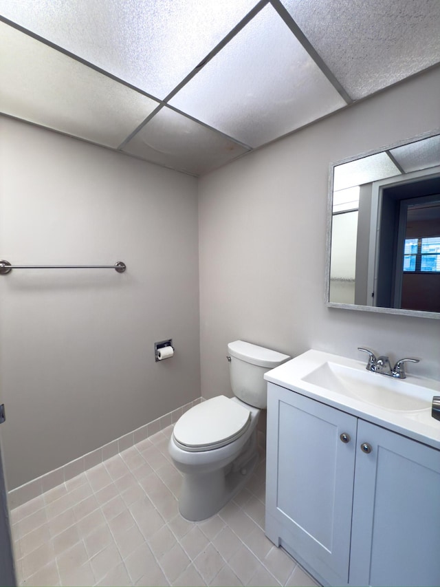 half bathroom with vanity, tile patterned floors, toilet, and a drop ceiling