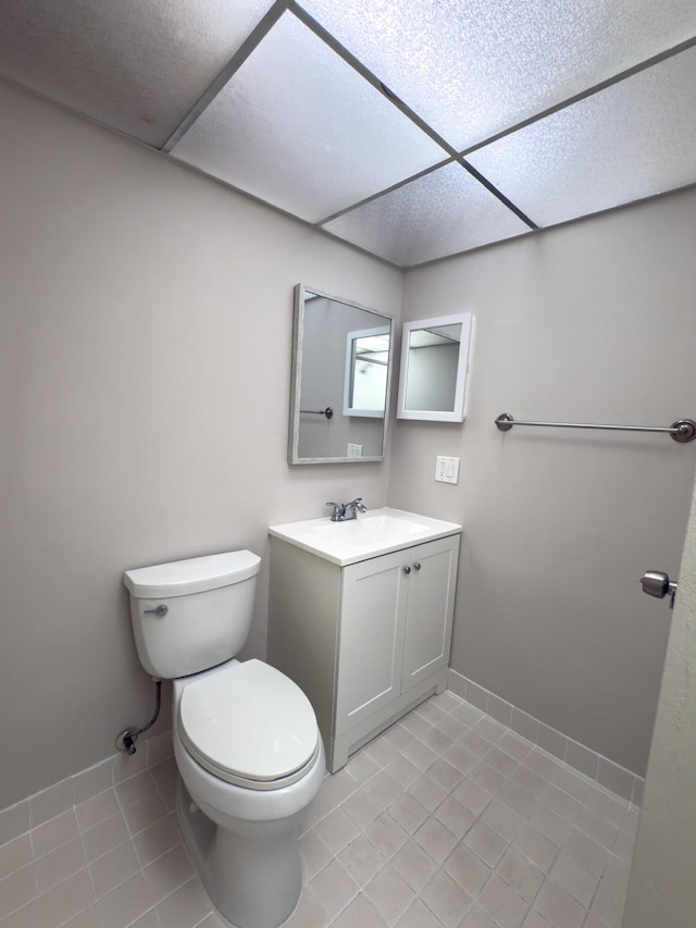 bathroom featuring tile patterned flooring, baseboards, a drop ceiling, toilet, and vanity