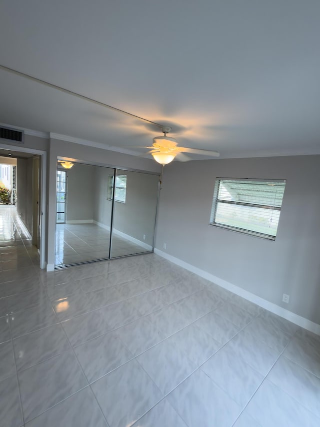 unfurnished bedroom featuring tile patterned flooring, visible vents, crown molding, ceiling fan, and baseboards