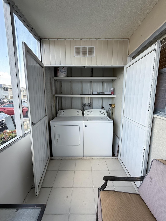 clothes washing area featuring washer and clothes dryer, visible vents, and a textured ceiling