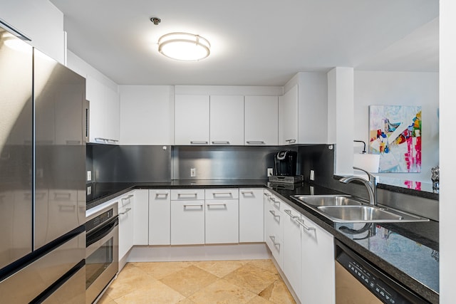 kitchen with dark countertops, white cabinetry, stainless steel appliances, and a sink