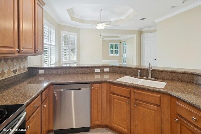 kitchen with dark stone counters, brown cabinets, stainless steel appliances, a raised ceiling, and a sink